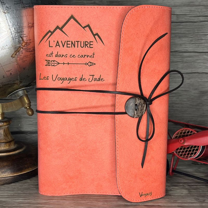Gravure personnalisée sur le carnet de voyage saumon posé sur un meuble